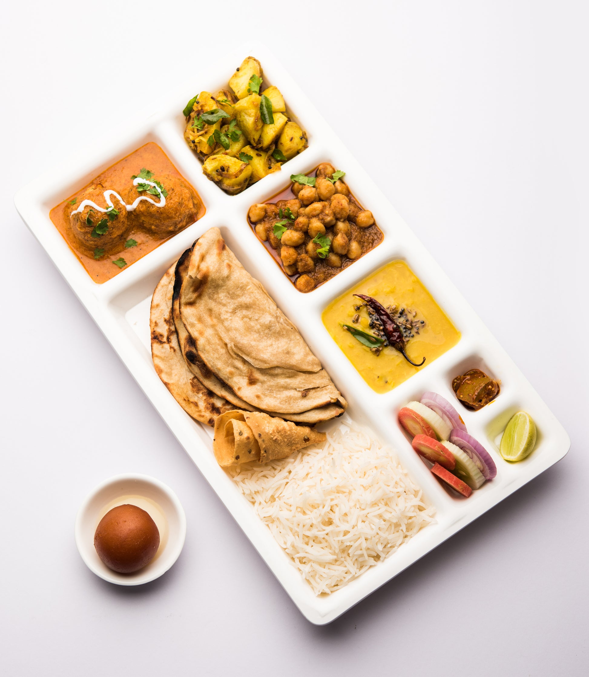 Platter of Indian food including rice, roti, and various dishes on a white background